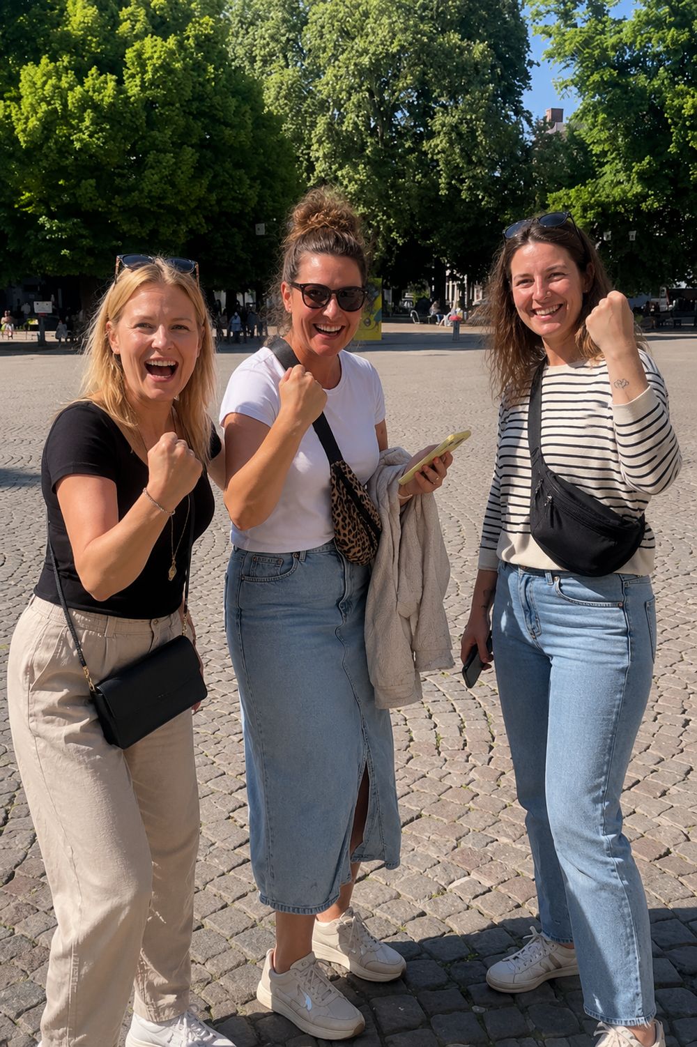 Drei Frauen auf einem Platz in Gent ballen die Faust, eine von ihnen mit einem Smartphone in der Hand