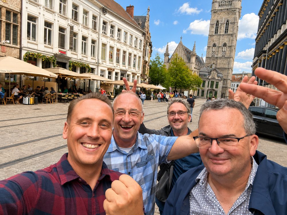 Vier spelers juichen op een plein in het centrum van Gent, met het Belfort op de achtergrond
