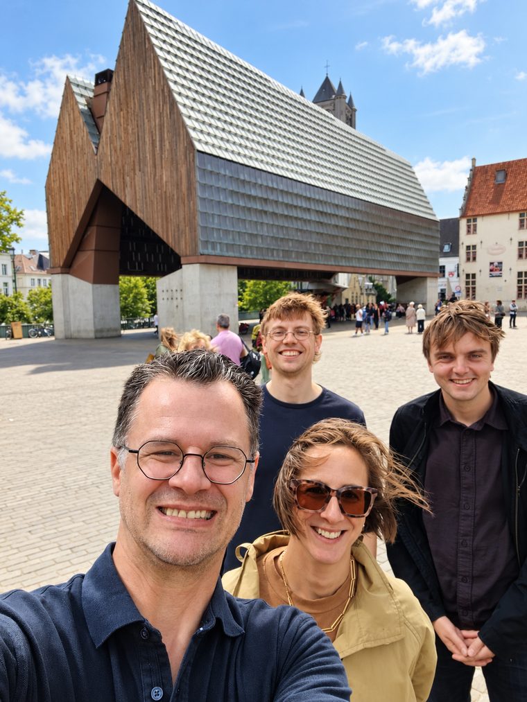 Vier spelers kijken lachend in de camera voor de Stadshal op het Emile Braunplein in Gent